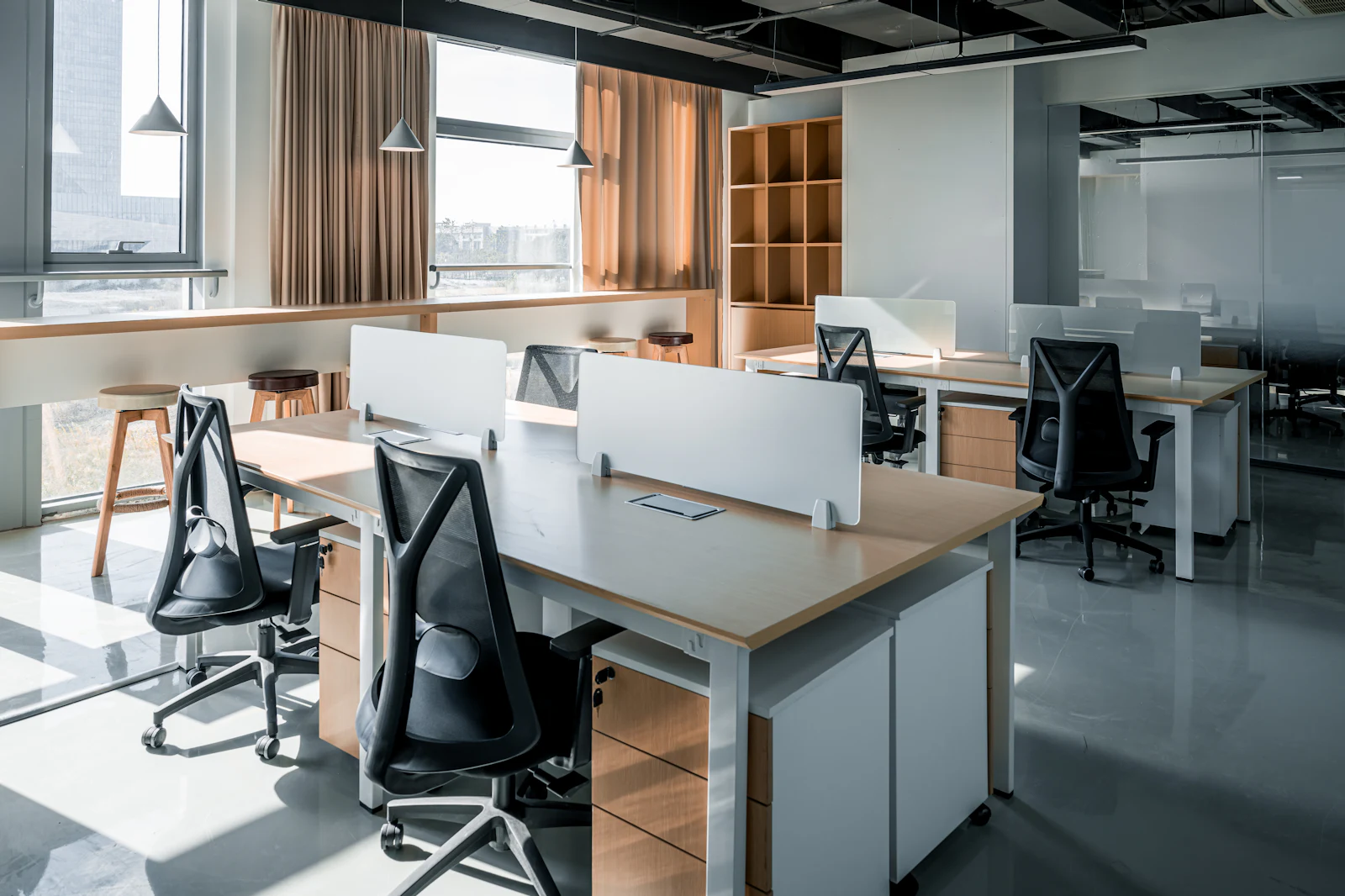 Presvetlená open-space kancelária s bielymi pracovnými stolmi pri oknách